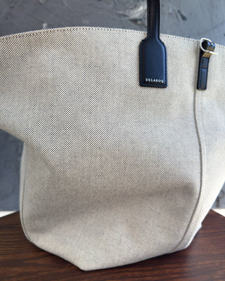 Beige tote bag with a visible brand tag on a wooden surface and gray background