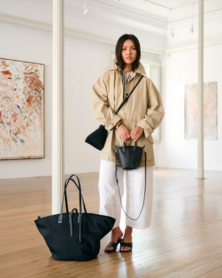 Woman in a beige coat holding black bags in an art gallery setting