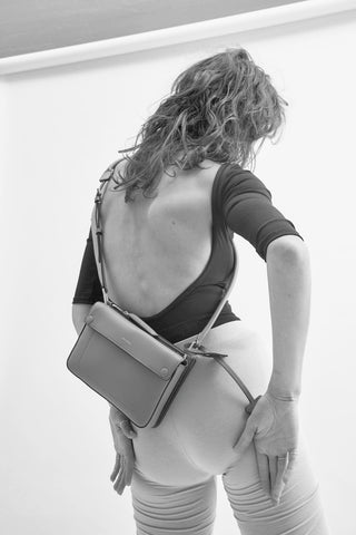 Person wearing a backless top and holding a handbag against a white background