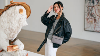Woman in a black leather jacket and white pants standing next to a large ceramic lion sculpture indoors.