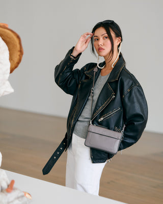 Woman wearing a black leather jacket with a gray handbag indoors.