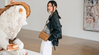 Woman in a stylish outfit with a leather jacket and beige handbag standing in an art gallery.