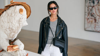 Woman in a black leather jacket and sunglasses standing in an art gallery.
