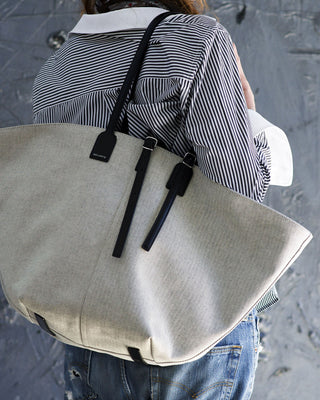 Person carrying a beige tote bag with black straps on a textured surface