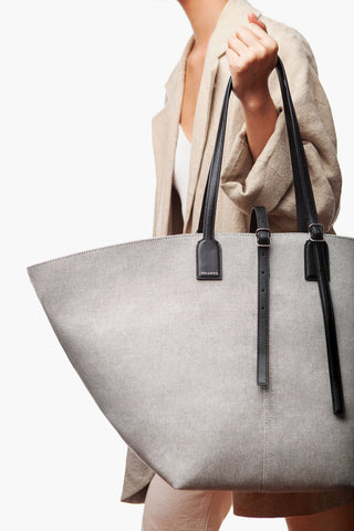 Gray tote bag with black handles held by a person wearing a beige coat.