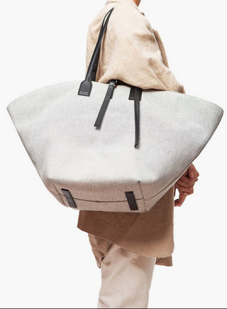 Person holding a large light gray tote bag with black straps on a white background