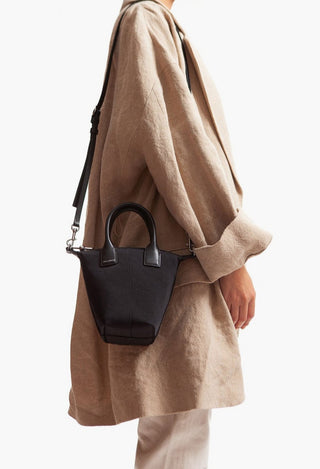 Person wearing a beige coat with a black handbag on a white background
