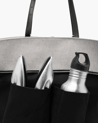 Black handbag with a water bottle and shoes in the interiorpocket on a white background