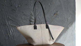 Beige handbag with black handle and strap on a gray textured background
