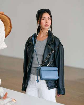 Woman wearing a black leather jacket and holding a blue handbag indoors.